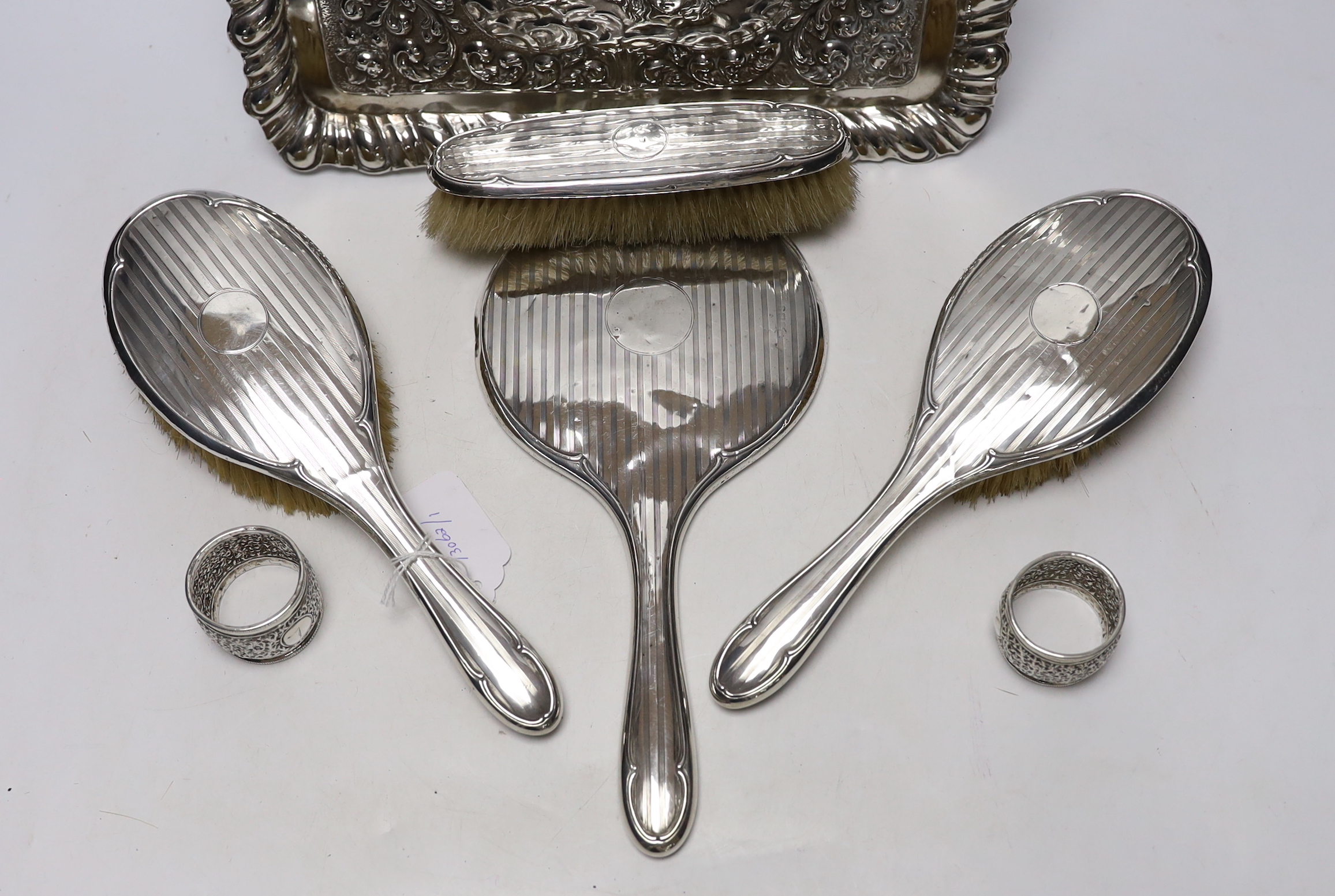 An Edwardian repousse silver dressing table tray, with Reynold's Angels decoration, Birmingham, 1904, 29.7cm, a silver dressing table mirror, two brushes, a clothes brush and two napkin rings.